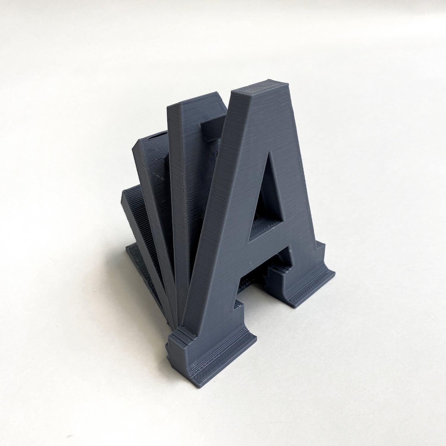The letter A, standing up strong with echoes of itself appearing to fall behind it. It is printed in a grey color.